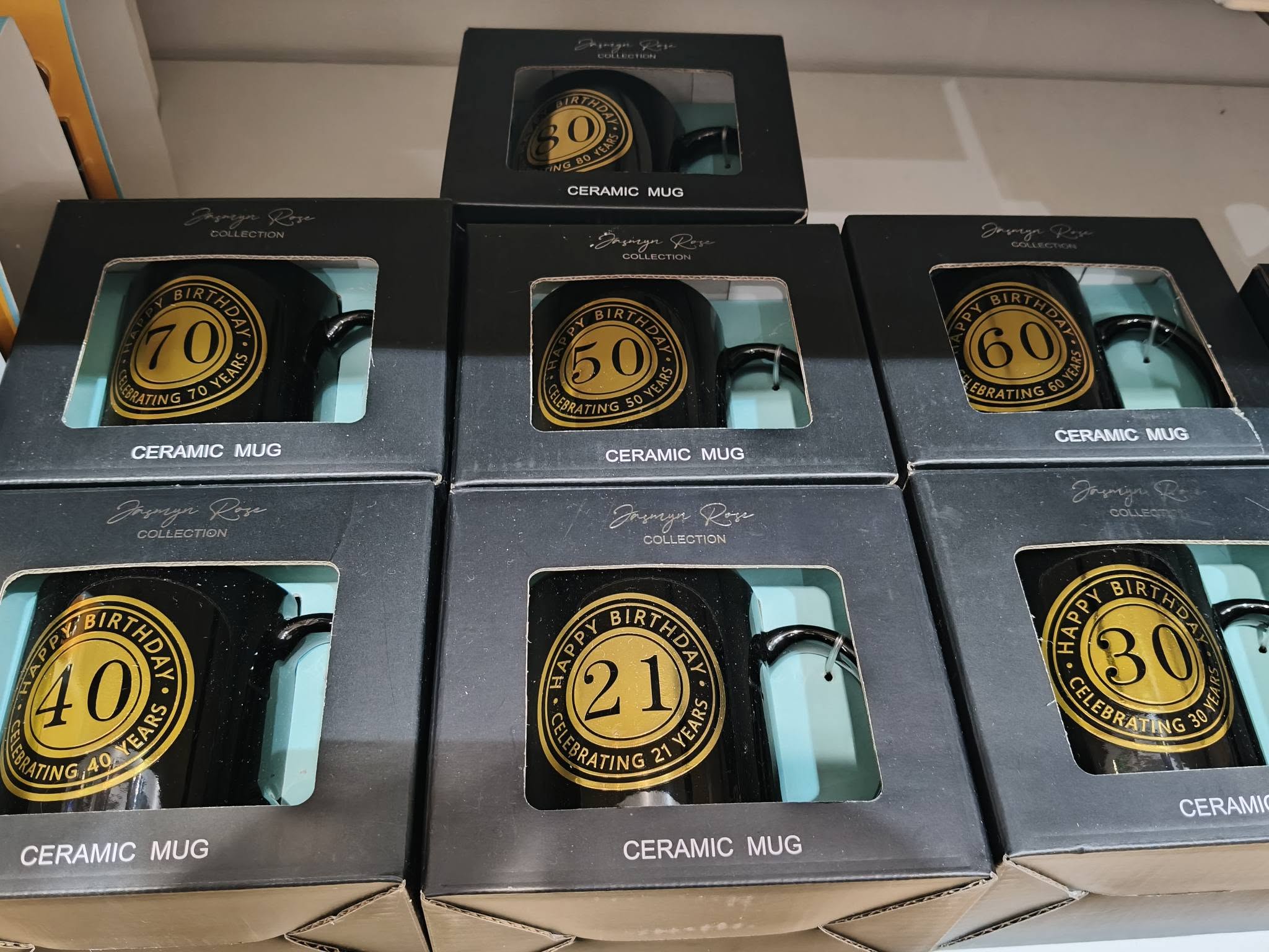 Black ceramic birthday mugs with gold milestone badges in boxed packaging